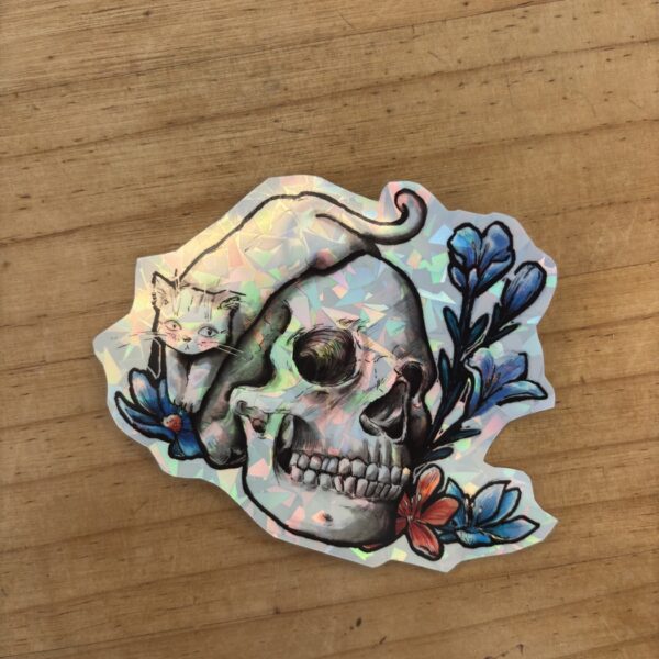 Sticker holographique illustré avec un crâne, un chat et des fleurs